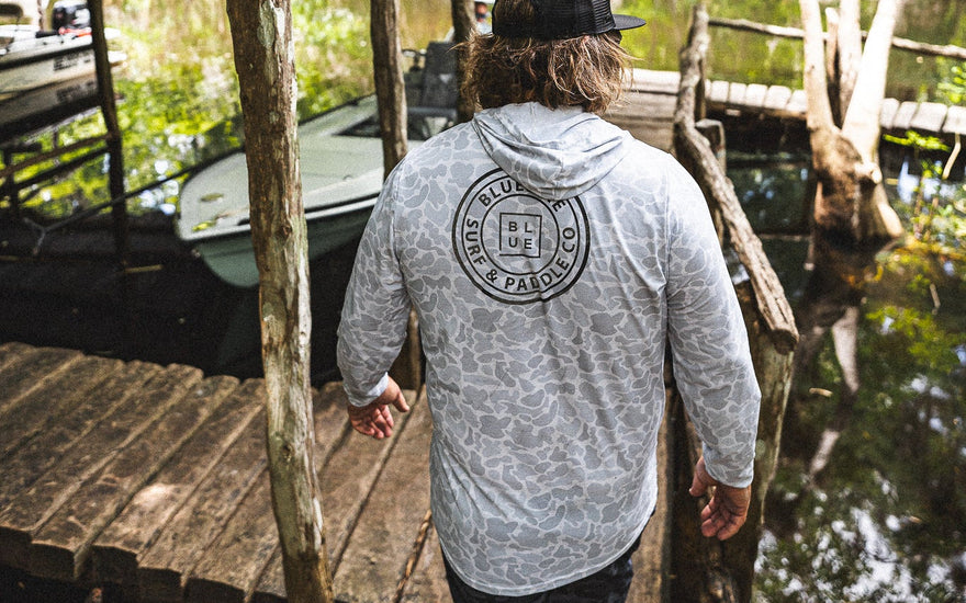 Man wearing a hooded men’s UV sun shirt on a dock at Blueline Surf and Paddle near Trapper Nelson’s on the Loxahatchee River in Jupiter, Florida