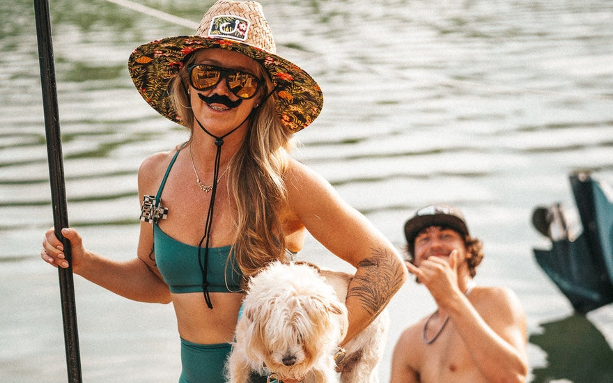 Paddleboarder wearing a sombrero and fake mustache holds a small dog while posing on the dock during the Cinco De Mayo themed Tuesday Night Race League event at Guanabanas in Jupiter, Florida.