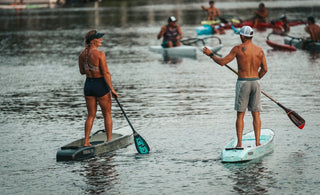 Paddlers racing during the final Tuesday Night Race League of 2026 in Jupiter, Florida as stand up paddleboards and surfskis move through the calm Intracoastal waterway at sunset behind Blueline Surf & Paddle Co.