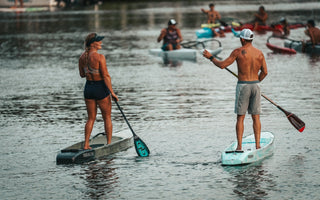 Paddlers racing during the final Tuesday Night Race League of 2026 in Jupiter, Florida as stand up paddleboards and surfskis move through the calm Intracoastal waterway at sunset behind Blueline Surf & Paddle Co.