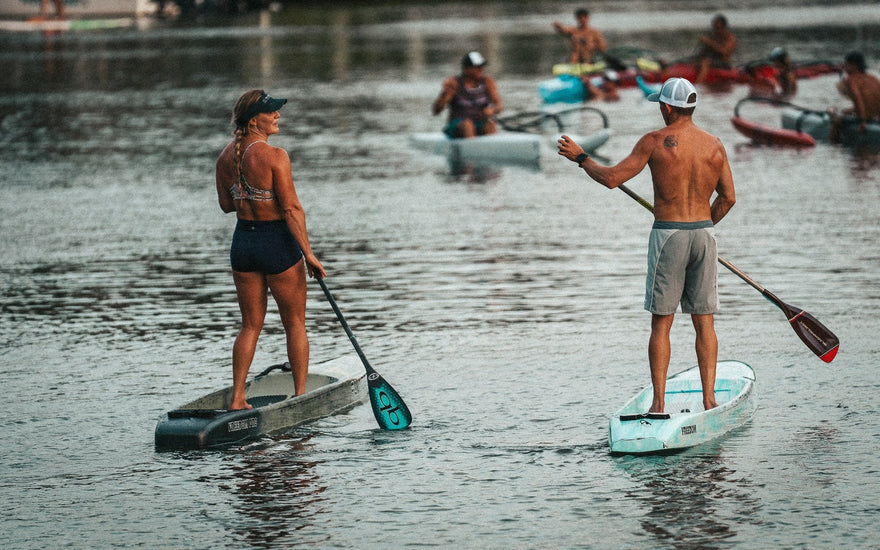 Paddlers racing during the final Tuesday Night Race League of 2026 in Jupiter, Florida as stand up paddleboards and surfskis move through the calm Intracoastal waterway at sunset behind Blueline Surf & Paddle Co.