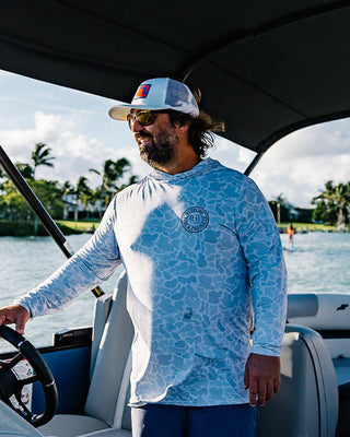 Man wearing a Blueline men’s UV sun shirt on a boat in Jupiter Florida with water and palm trees in the background