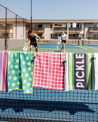 Nomadix fitness and yoga towels hanging courtside during a pickleball match, featuring quick-dry performance towels designed for yoga, gym workouts, racket sports, and active lifestyles.