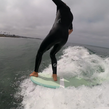 Person in a wetsuit standing on a surfboard riding a wave in the ocean.