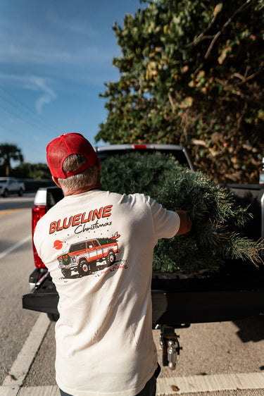 Man loading a Christmas tree into a truck wearing a 'Blueline Christmas' t-shirt in Jupiter Florida
