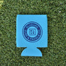 Neon blue Blueline Surf & Paddle Co. neoprene koozie with navy logo on grass