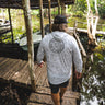 Man wearing a heather smoke camo Blueline OG Circle UV sun hoodie walking on a dock in Jupiter, Florida.