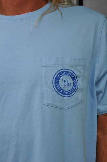 Light blue shirt with a pocket Blueline Surf and Paddle Co. logo on the chest pocket, worn by a person.