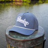 Blueline Kids Surfboard Tech Hat in slate and White displayed on a dock in Jupiter, Florida.