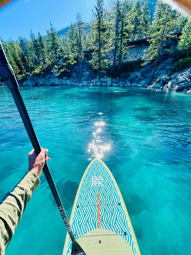Person paddleboarding on clear blue water with a forested shoreline
