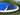 A blue and white stand-up paddleboard with a dark textured grip pad, photographed outdoors on grass with green foliage and water in the background.