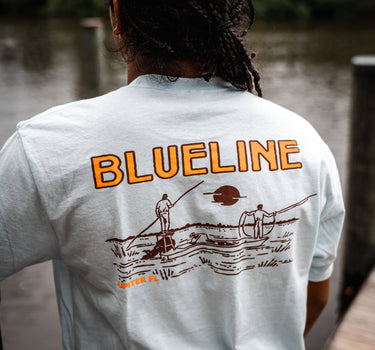 Image of the Blueline Surf & Paddle Co. fly fishing T-shirt featuring a guide poling on a skiff with an angler casting at sunset in Jupiter, Florida. The back drop is the intracoastal in Palm Beach County Florida.