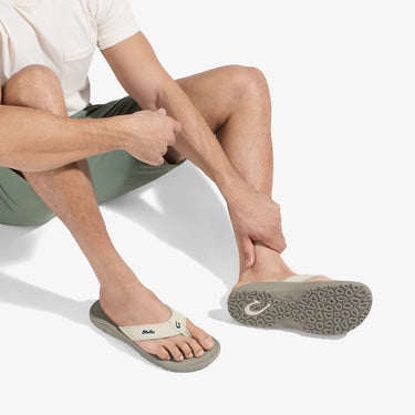 Man wearing OluKai ʻOhana Tapa Clay sandals while relaxing aboard a boat, showcasing premium comfort and water-friendly performance.