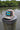 Camo Bahamas flag trucker hat by Blueline Surf & Paddle photographed on a weathered dock piling overlooking calm waterfront waters in Jupiter Florida.