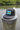 Black Bahamas flag trucker hat by Blueline Surf & Paddle photographed on a weathered dock piling overlooking calm Jupiter Florida waterfront waters.