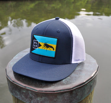Navy and white Bahamas flag trucker hat by Blueline Surf & Paddle photographed on a dock piling overlooking the Jupiter Florida waterfront.