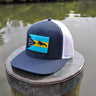 Navy and white Bahamas flag trucker hat by Blueline Surf & Paddle photographed on a dock piling overlooking the Jupiter Florida waterfront.