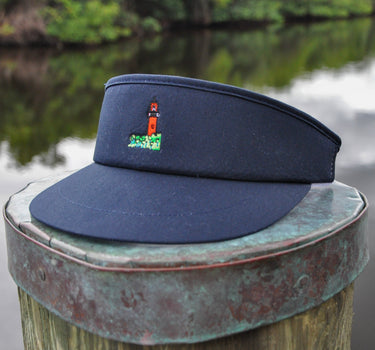 Navy Imperial Tour Visor featuring an embroidered Jupiter Lighthouse on the front and a classic high-profile design, photographed on a dock piling in Jupiter, Florida.
