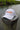 The Blueline America 250 performance hat in white featuring a clean, rope-free front profile, displayed on a weathered wood piling along the water in Jupiter, Florida.