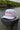The Blueline America 250 performance rope hat in white from the Americana Edit collection, displayed on a wooden dock piling along the Intracoastal water in Jupiter, Florida.
