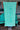 Blueline Beach Towel in mint green with vertical Blueline logo displayed outdoors at Blueline Surf & Paddle Co. in Jupiter, Florida.