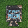 Tree camo neoprene Blueline Hunt Club koozie with light blue boar hog and palmetto graphic displayed on grass