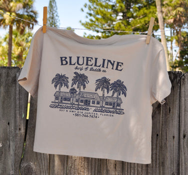 Women's Blueline Jupiter Shop Crop T-Shirt in bone featuring a pale navy coastal surf shop graphic inspired by Jupiter, Florida.