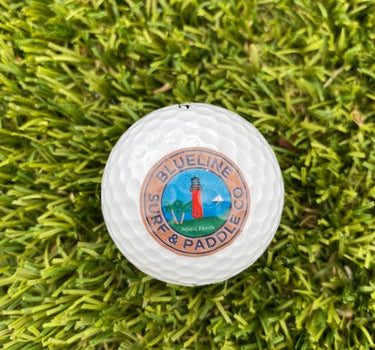 Blueline Lighthouse logo golf ball resting on green grass, featuring the Jupiter Lighthouse design.