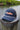 The Blueline Navy performance rope hat from the Americana Edit collection, displayed on a wooden dock piling along the Intracoastal water in Jupiter, Florida.