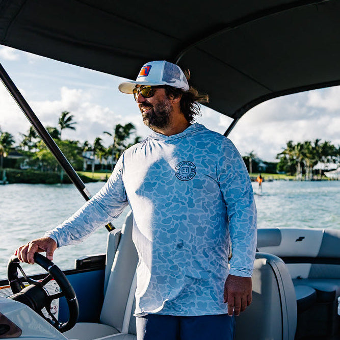 Man steering a boat, surrounded by water and trees.