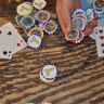 Hand holding Blueline poker chip style golf ball markers on a wooden table with playing cards and chips in the background.