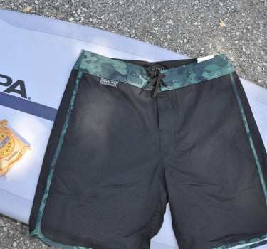 Blueline Sideline performance boardshorts in Black and Squid Camo laid across a surfboard.