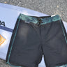 Blueline Sideline performance boardshorts in Black and Squid Camo laid across a surfboard.