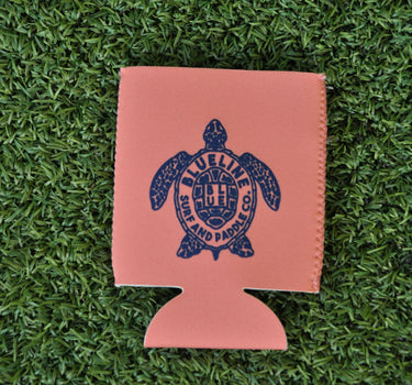Pink neoprene Blueline turtle logo koozie with navy print displayed on grass