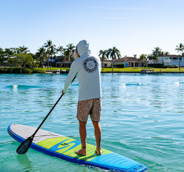 Man paddleboarding on clear blue water wearing a light blue Blueline Vintage Circle Low Pro UV sun hoody.