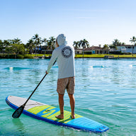 Man paddleboarding on clear blue water wearing a light blue Blueline Vintage Circle Low Pro UV sun hoody.