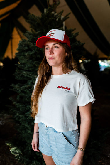 Person wearing a white blueline christmas t-shirt and a red hat, standing outdoors in a christmas tree farm.