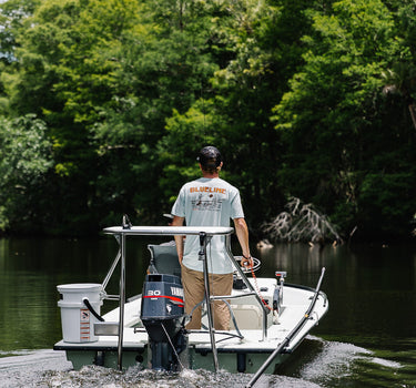 Person wearing a Blueline Surf & Paddle shirt driving a small boat on the Loxahatchee River in Jupiter, Florida, representing the South Florida lifestyle and life on the water that defines the Blueline brand.