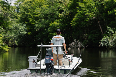 Person wearing a Blueline Surf & Paddle shirt driving a small boat on the Loxahatchee River in Jupiter, Florida, representing the South Florida lifestyle and life on the water that defines the Blueline brand.