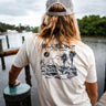 Man wearing a washed natural Blueline Gator Lasso T-shirt with light navy artwork while standing on a dock near the water in Jupiter, Florida.