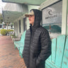 Man wearing ID Simmons black hooded puffy jacket outside surf shop