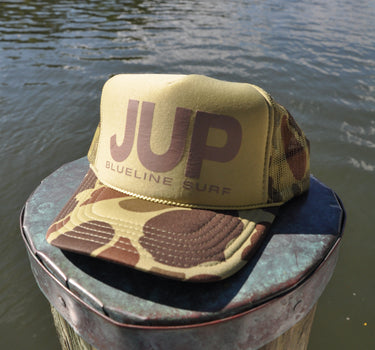 JUP Trucker Hat Tan/Camo with bold JUP lettering and camo brim on dock in Jupiter Florida