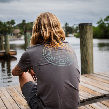 Man sitting on the docks at Guanabanas in Jupiter, FL wearing a blueline asphalt shirt back view.