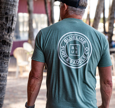 Back view of a canyon green Blueline OG logo T-shirt with large white circle logo, photographed outdoors in Jupiter, Florida.