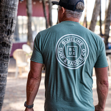 Back view of a canyon green Blueline OG logo T-shirt with large white circle logo, photographed outdoors in Jupiter, Florida.