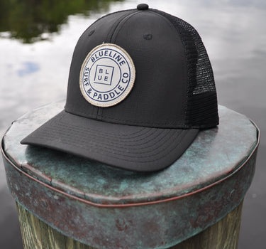 OG Blueline Logo UV Lite Hat in Black with stone patch displayed on a dock piling