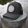 OG Blueline Logo UV Lite Hat in Black with stone patch displayed on a dock piling