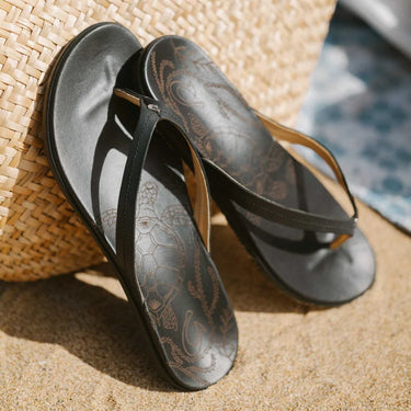 Women's OluKai Honu Black leather sandals styled for beach vacations, travel, and everyday coastal wear.