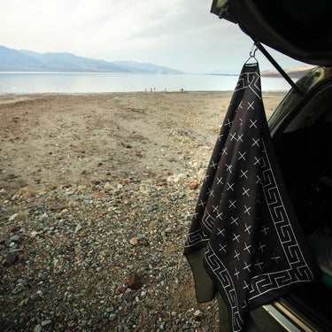 Black towel with white patterns hanging from a car window over a desert landscape.