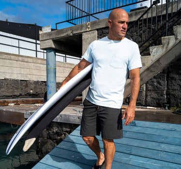 Kelly Slater wearing Outerknown UPF 50 sun shirt walking with Surfboards.